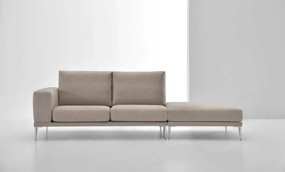 Sofá beige con chaise longue y patas cromadas, fotografiado en estudio sobre fondo blanco