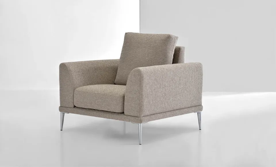Sillón beige con patas cromadas, fotografiado en estudio sobre fondo blanco