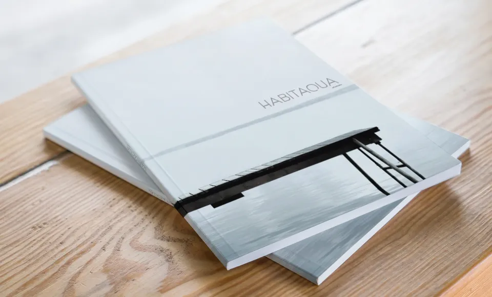 Two Habitacua catalogues stacked on a wooden table with a jetty photo on the cover
