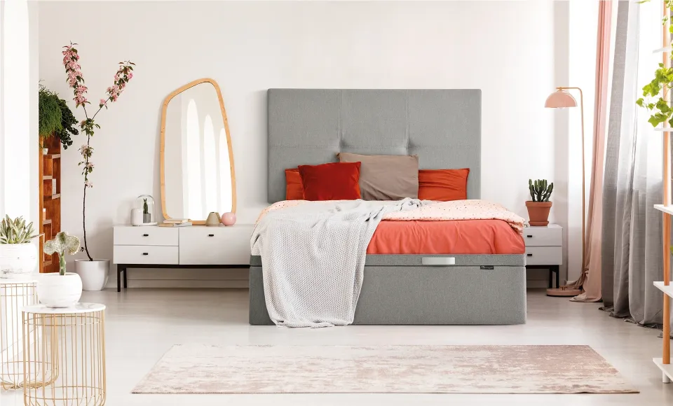 Bedroom with a grey-upholstered bed and cushions in orange and red tones
