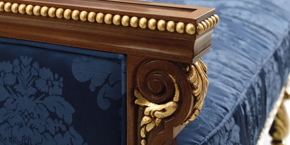 Detalle del brazo tallado y dorado de un sofá con tapizado azul estampado