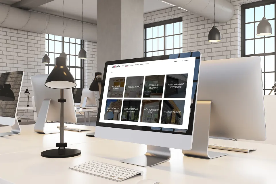 Desktop computer showing LaViuda's website with a grid of categories, in a brick-walled office