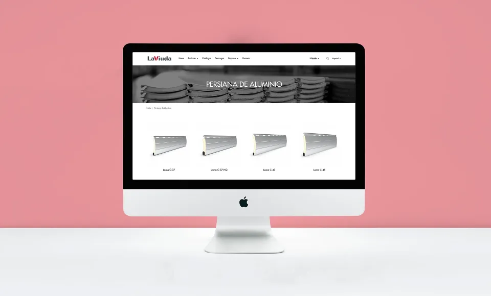 Ordenador con la web de LaViuda mostrando el listado de persianas de aluminio, sobre fondo rosa