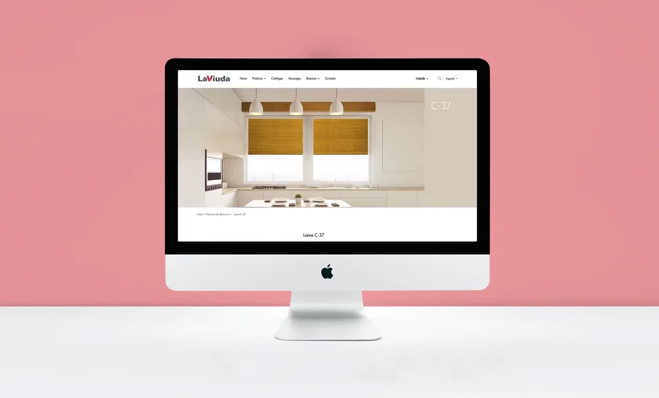 Ordenador con la web de LaViuda mostrando una cocina con persianas venecianas, sobre fondo rosa