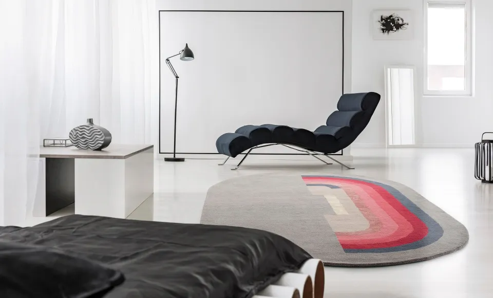Striped oval rug next to a dark chaise longue by Parentesi Quadra
