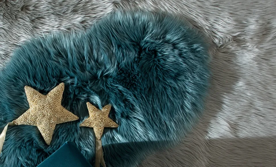 Teal faux-fur cushion with gold stars on a grey fur rug