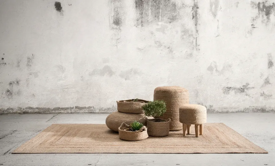 Parentesi Quadra woven baskets and a pouffe on a jute rug against a concrete wall