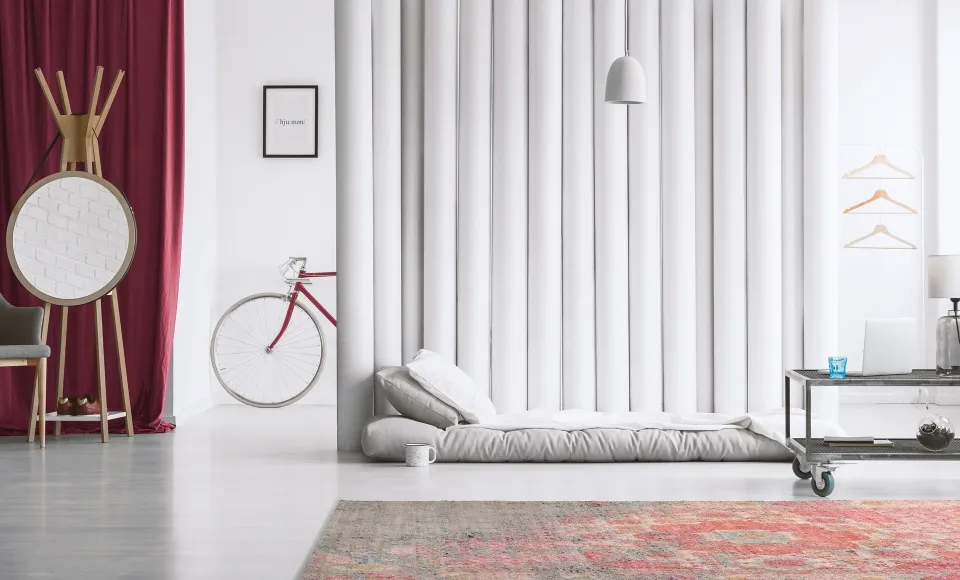 Parentesi Quadra red patterned rug next to a floor mattress and a bicycle